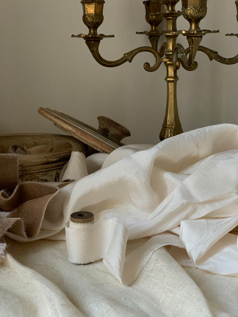 A classic still life featuring an antique brass candlestick, draped fabrics, and rustic elements.