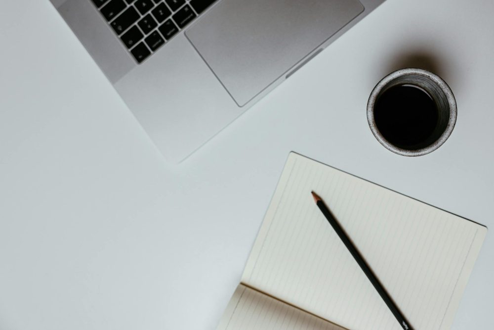 A clean, minimalist desk setup featuring a laptop, notebook, and coffee cup for productive work.