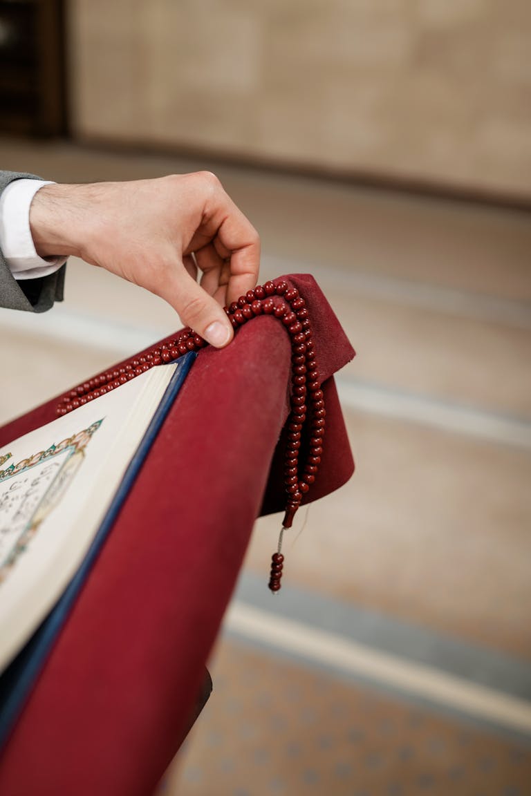 A close-up of a person's hand holding a Quran and prayer beads, symbolizing Islamic faith and devotion.