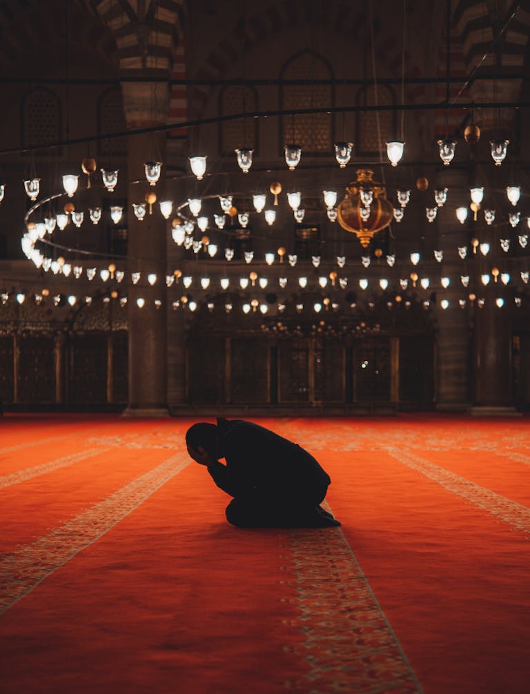 A man in silhouette kneels in prayer inside a beautifully illuminated mosque in Istanbul.