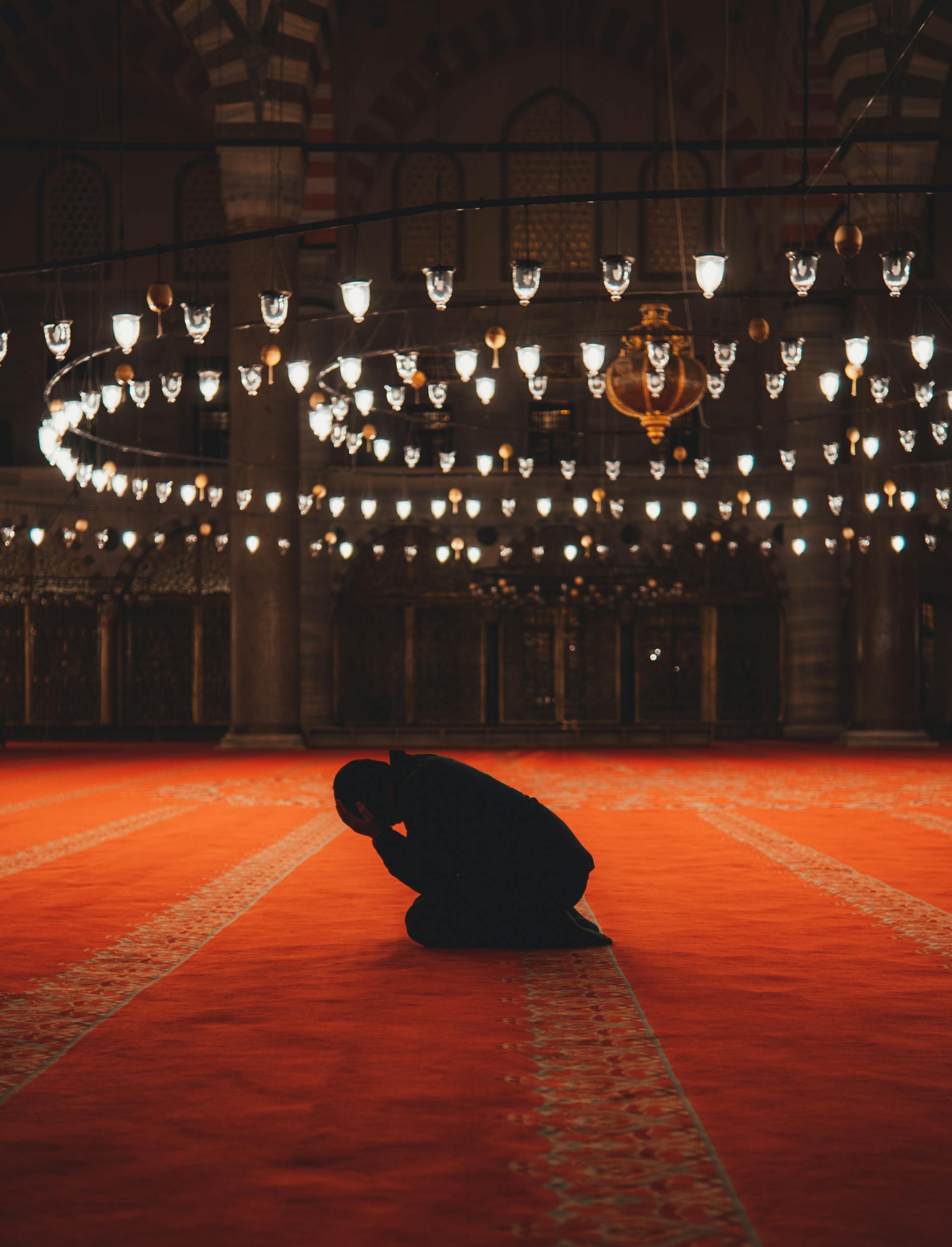 A man in silhouette kneels in prayer inside a beautifully illuminated mosque in Istanbul.