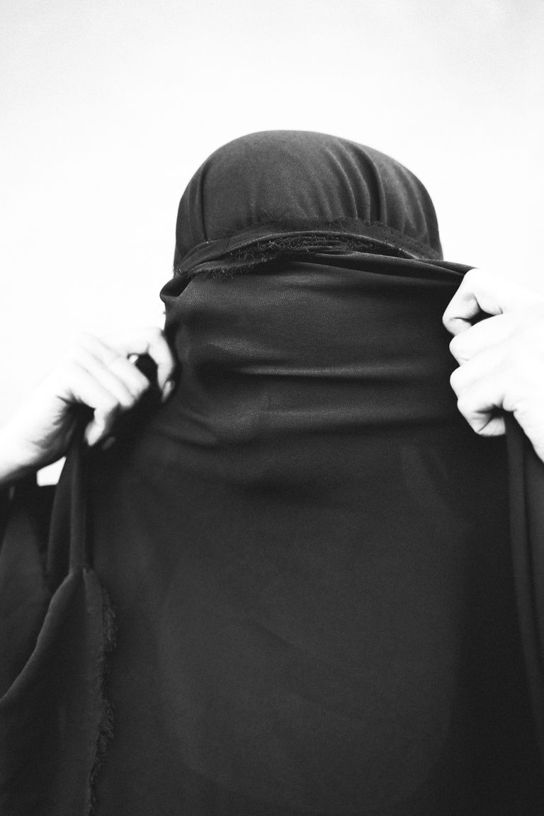 A monochrome close-up of a woman adjusting her veil, symbolizing faith and culture.