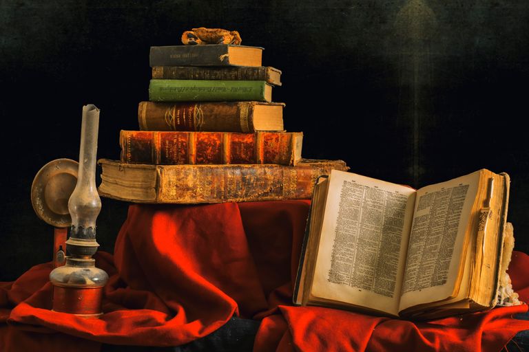 An artistic still life featuring a stack of vintage books and an olive lamp on rich red cloth.