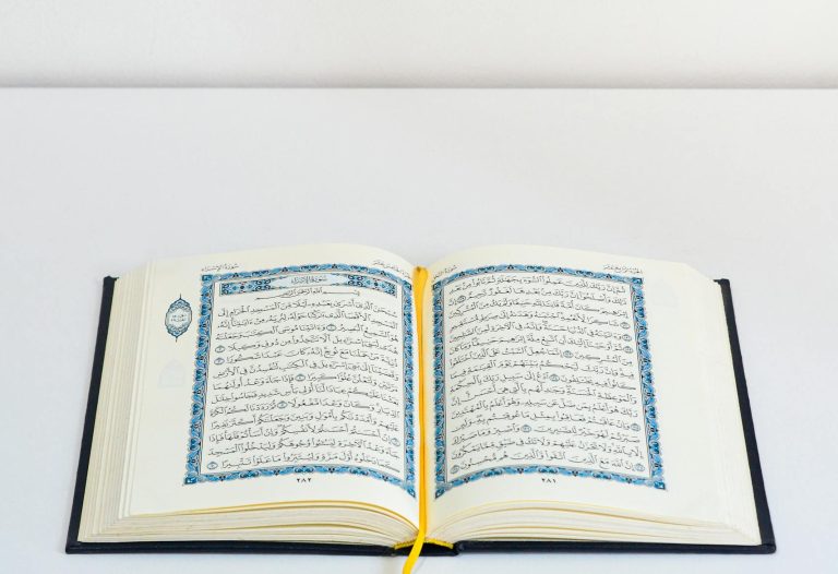 An open Quran on a white table with a yellow bookmark, photographed in a studio setting.