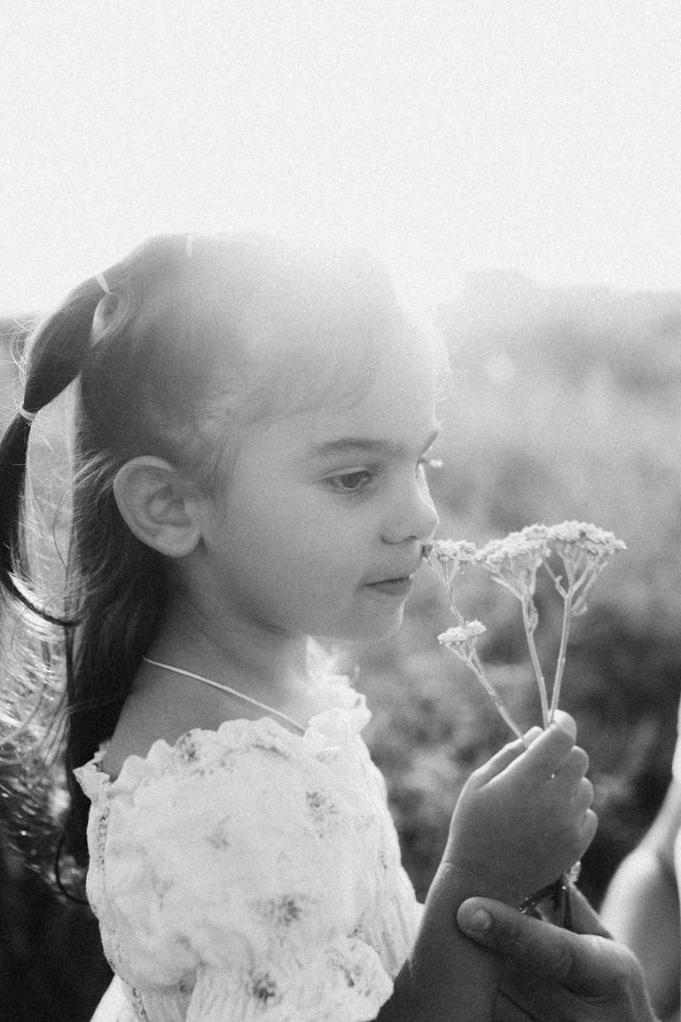 Black and white portrait of a young girl holding flowers in a sunlit field.