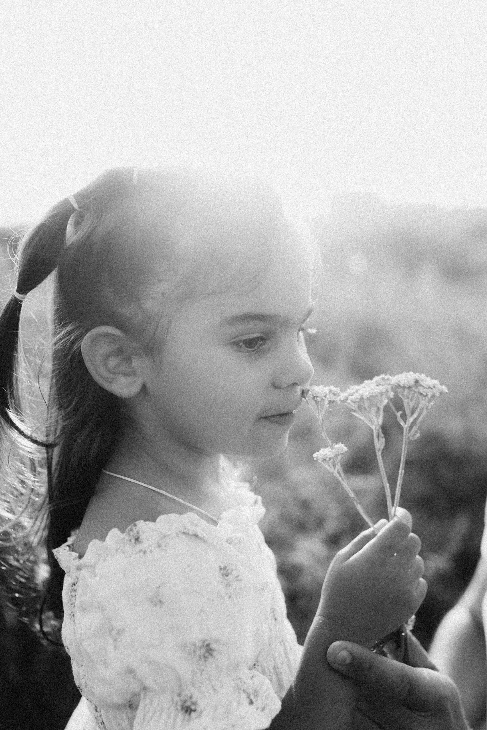 Black and white portrait of a young girl holding flowers in a sunlit field.