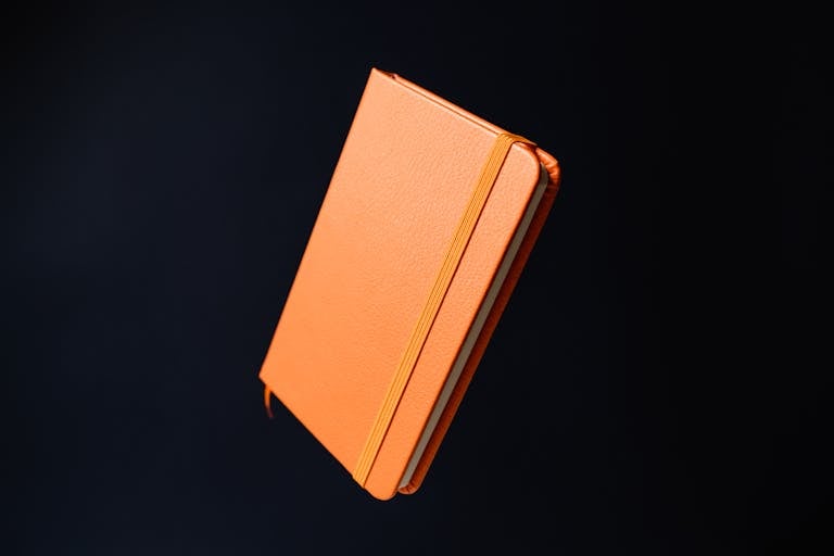 Close-up of an orange notebook floating against a dark backdrop, studio shot.