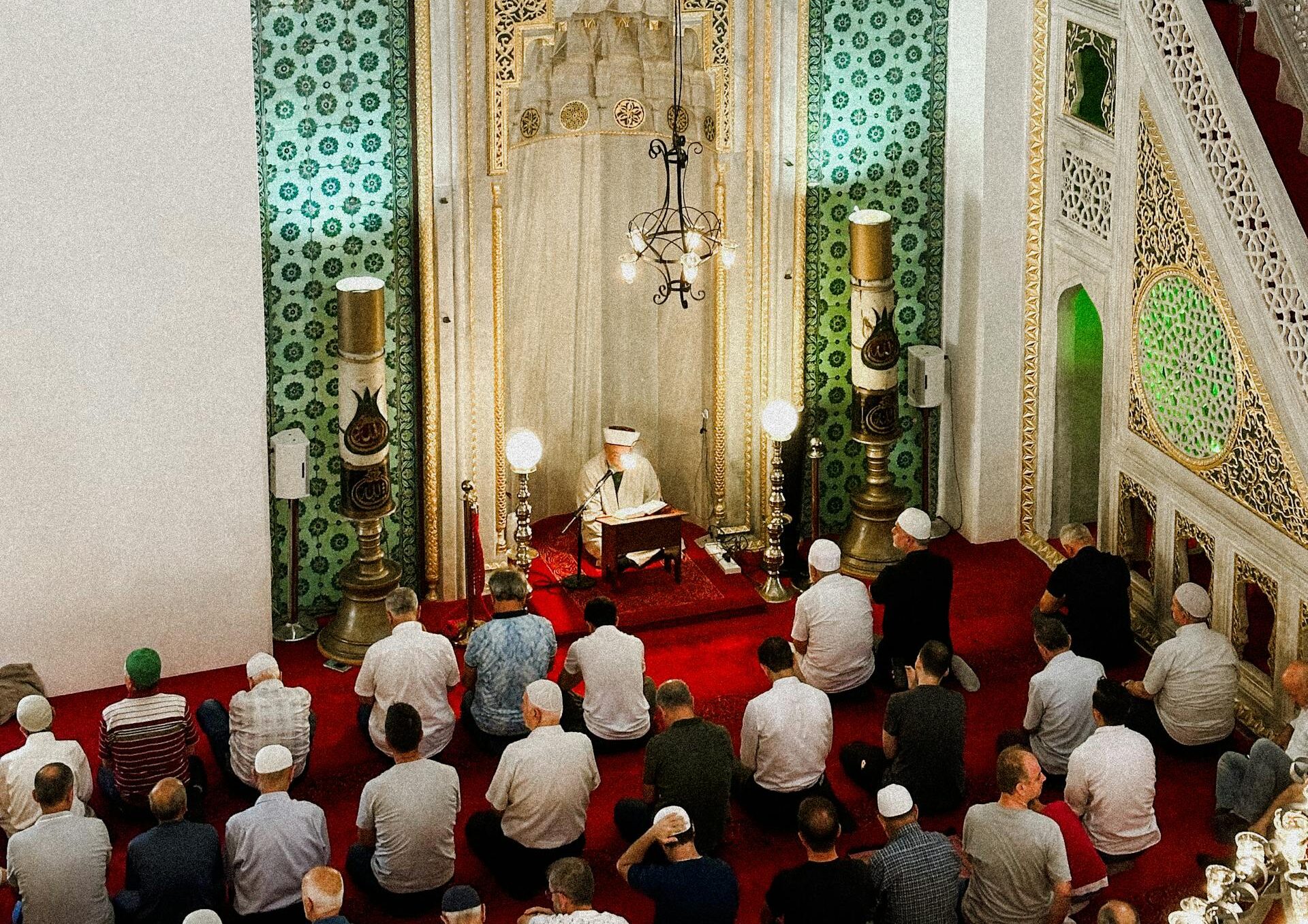 Group of people praying inside a beautifully ornate mosque with intricate Islamic designs.