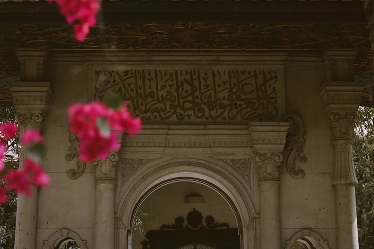 Ornate Islamic arch with calligraphy surrounded by vibrant pink bougainvillea.