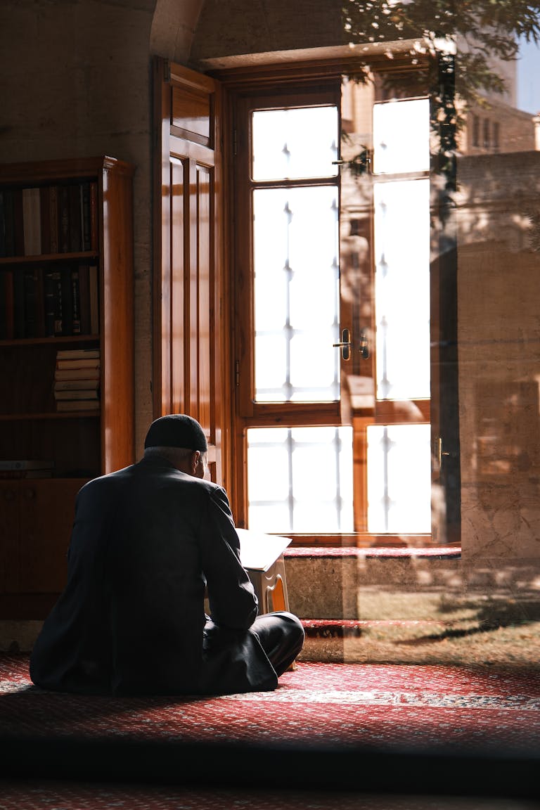 Silhouette of a man praying indoors in a sunlit room with traditional decor.