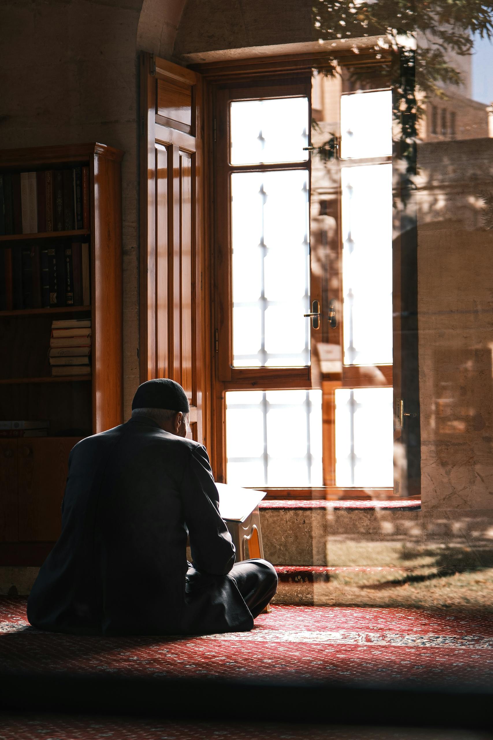 Silhouette of a man praying indoors in a sunlit room with traditional decor.