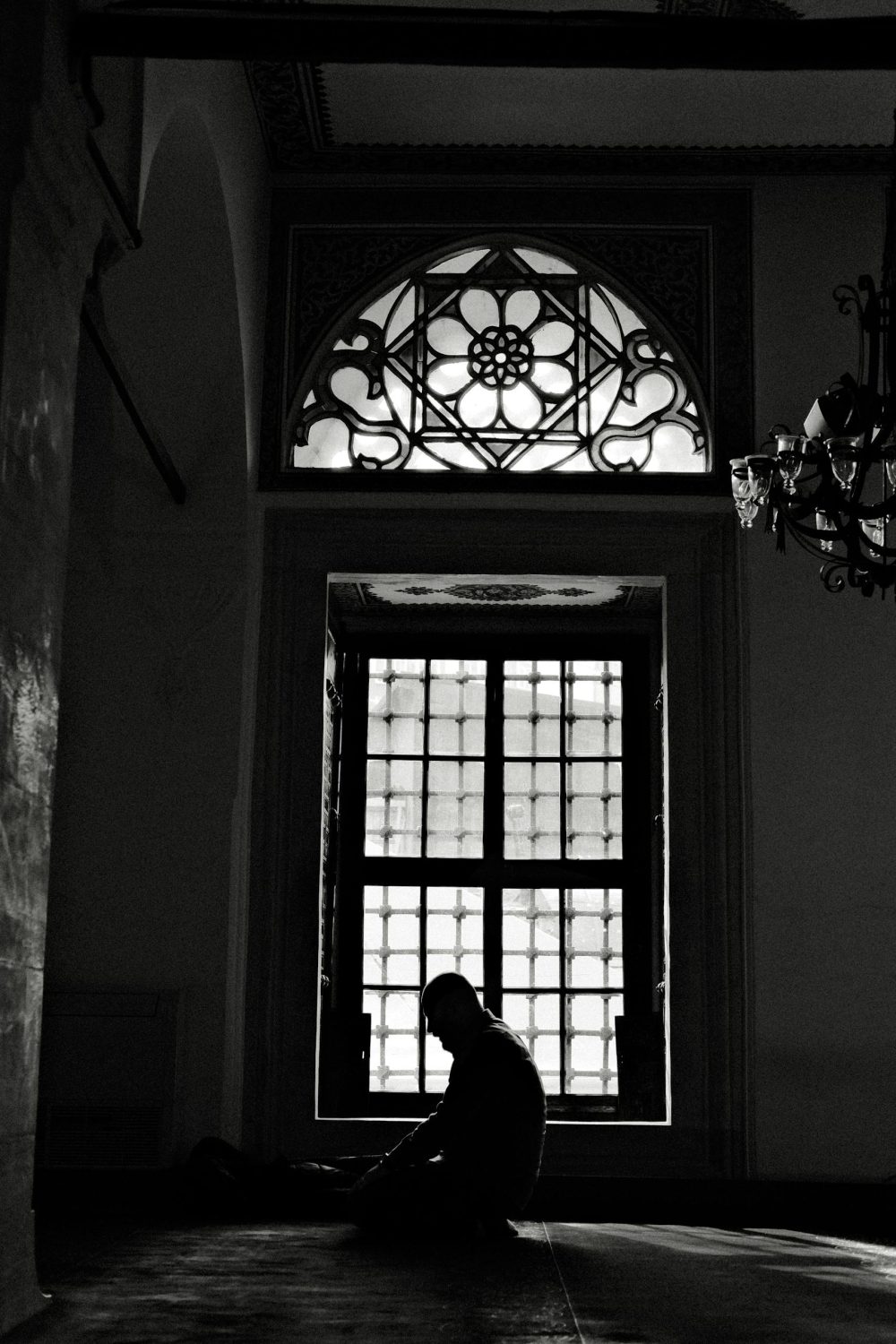 Silhouette of a man praying inside a mosque with stained glass window in İstanbul.